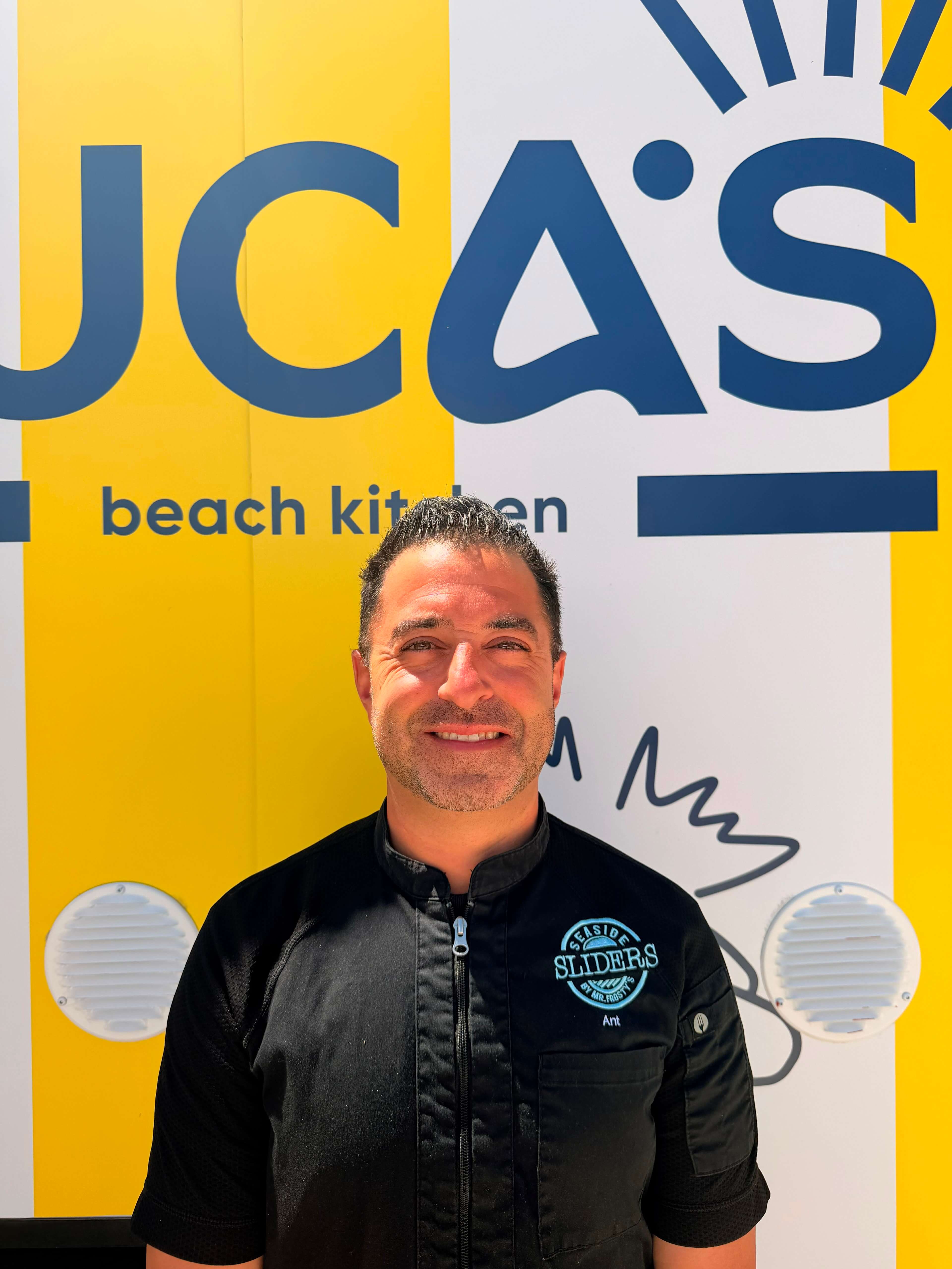 Anthony Luciani standing in front of the Luca's Beach Kitchen branding